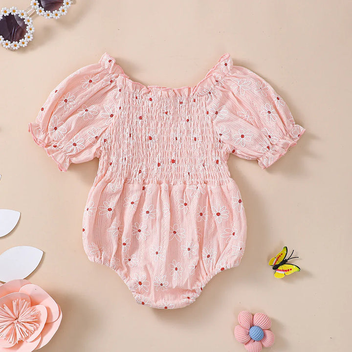 Pink baby romper with white and red daisy embroidery and puff sleeves on beige background