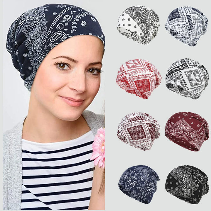 Woman wearing navy blue paisley bandana headscarf next to eight different colored paisley headscarves on gray background