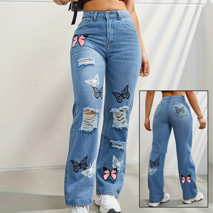 High-waisted blue ripped jeans with butterfly and pink bow patches, worn with white sneakers