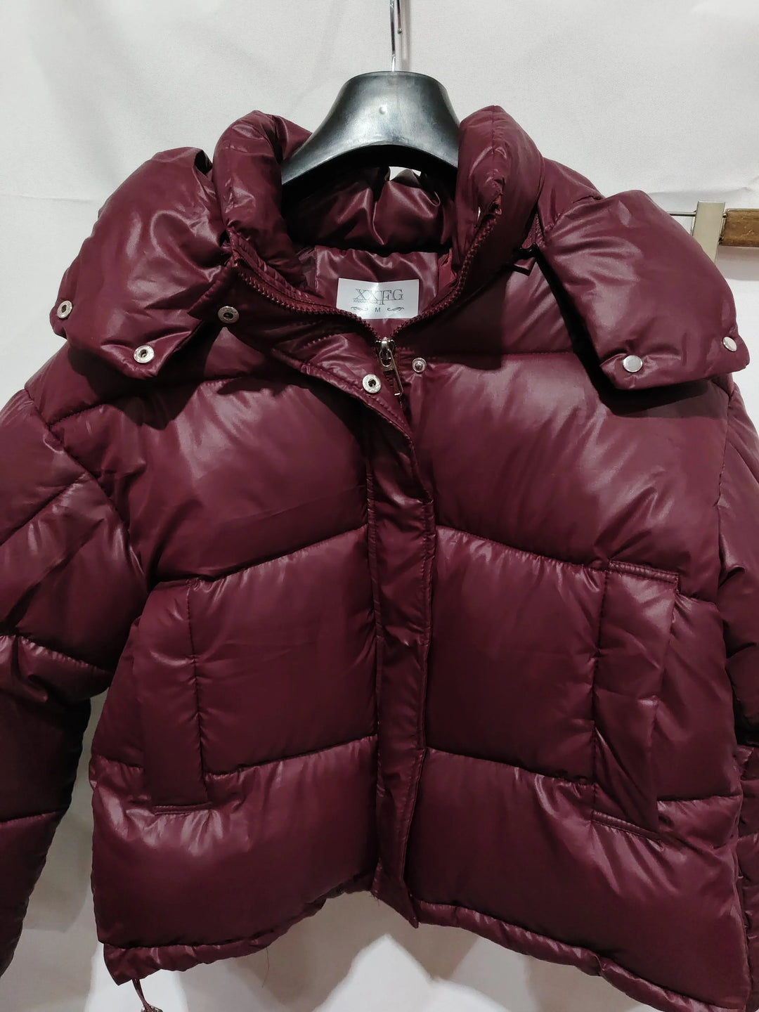 Maroon puffer jacket with high collar and snap buttons on hanger