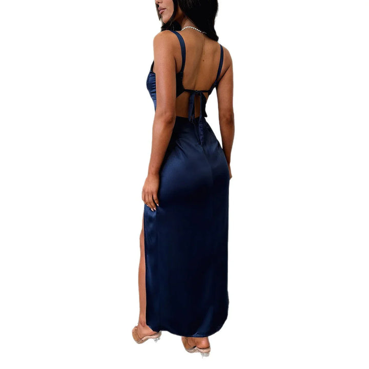 Woman wearing a navy blue satin backless maxi dress with tie-back and slit, styled with clear heels