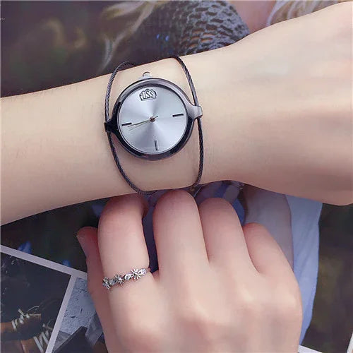 Minimalist wristwatch with a silver dial and black case worn on wrist with delicate ring featuring flower designs
