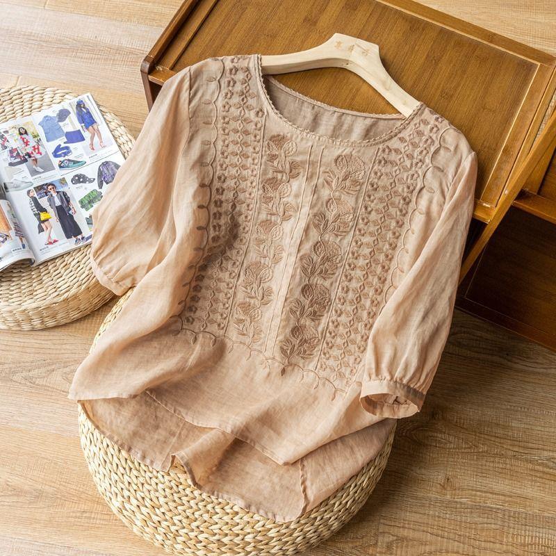 Beige embroidered blouse with floral patterns on wooden hanger on round woven mat and wooden floor