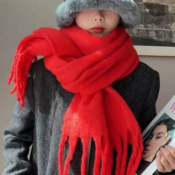 Person wearing oversized bright red scarf and gray fur hat with gray coat, holding magazine indoors