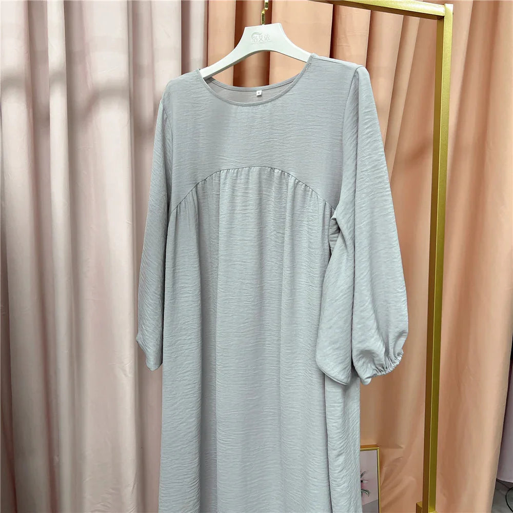 Light gray long-sleeve dress with gathered detail on hanger against beige curtains
