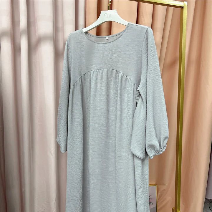 Light gray long-sleeve dress with gathered detail on hanger against beige curtains