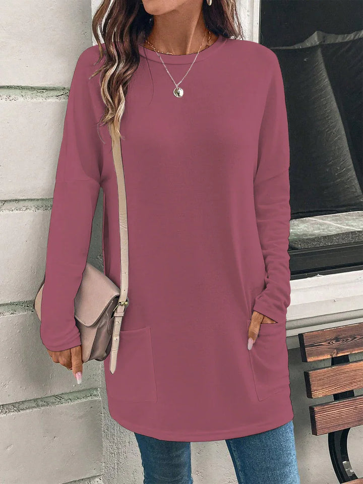 Woman wearing long sleeve mauve tunic top with front pockets and beige crossbody purse