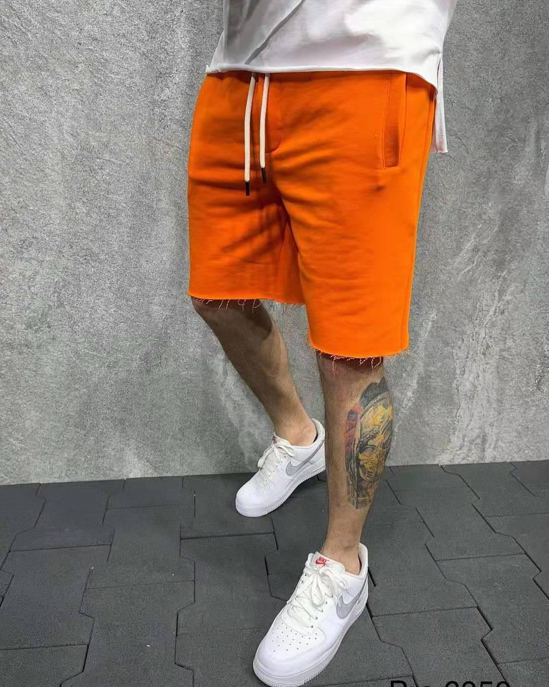 Man wearing bright orange casual shorts with frayed hem, white Nike sneakers, and tattooed leg