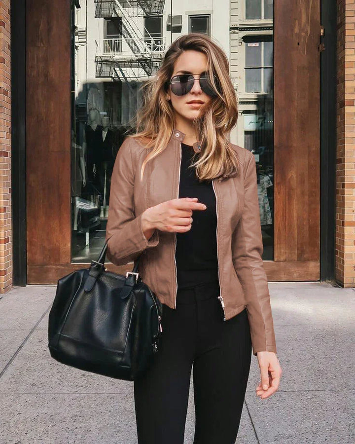 Stylish woman wearing brown leather jacket and black pants carrying black leather handbag on city street