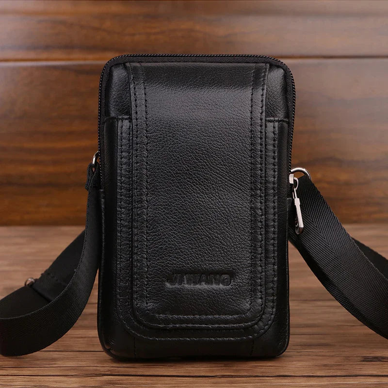 Black leather crossbody bag with zipper and adjustable strap on wooden surface