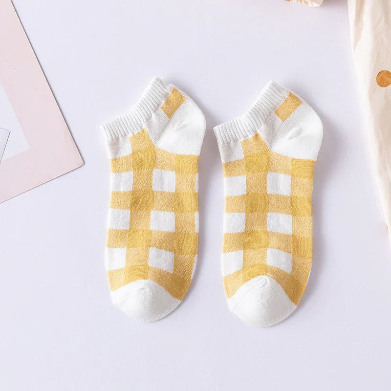 Pair of white ankle socks with yellow checkered pattern on a light surface
