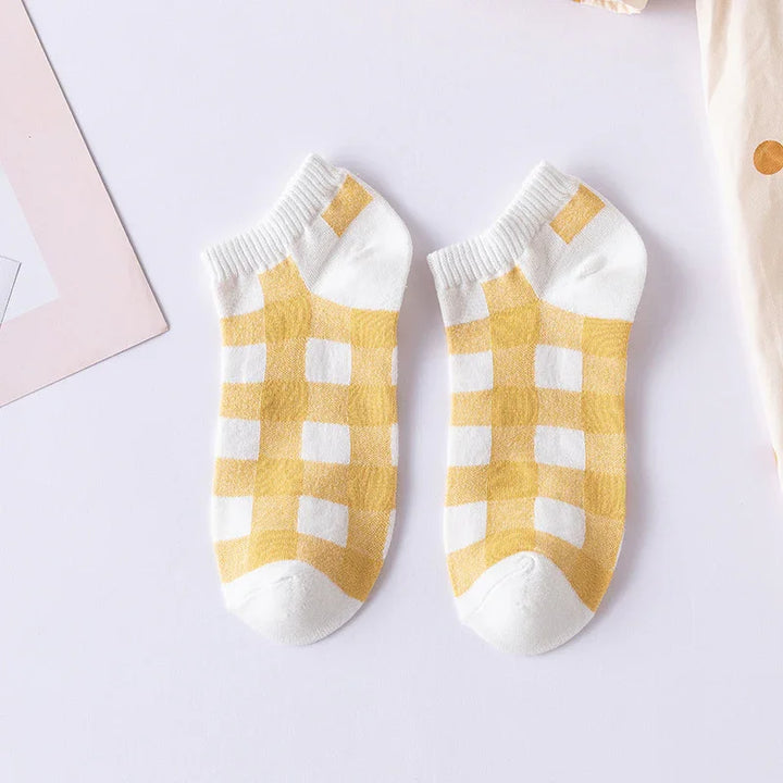 Pair of white ankle socks with yellow checkered pattern on a light surface