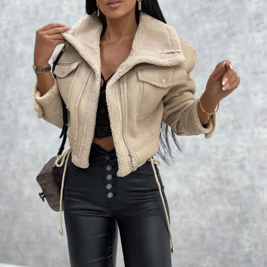 Woman wearing beige sherpa-lined cropped jacket with black lace crop top and high-waist black button pants