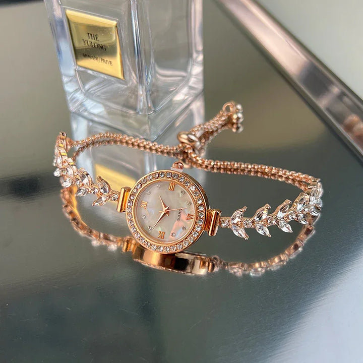 Elegant rose gold women's wristwatch with crystal accents on a reflective surface next to perfume bottle