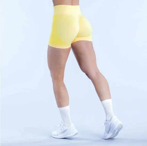 Woman wearing yellow seamless workout shorts, white socks, and white sneakers, studio background