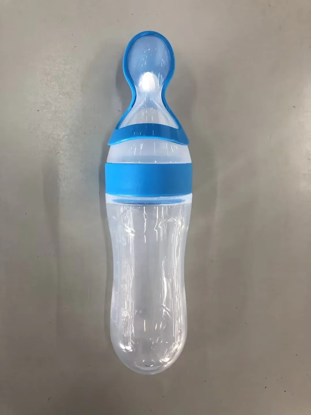 Clear plastic baby feeding bottle with blue silicone nipple and grip on gray background