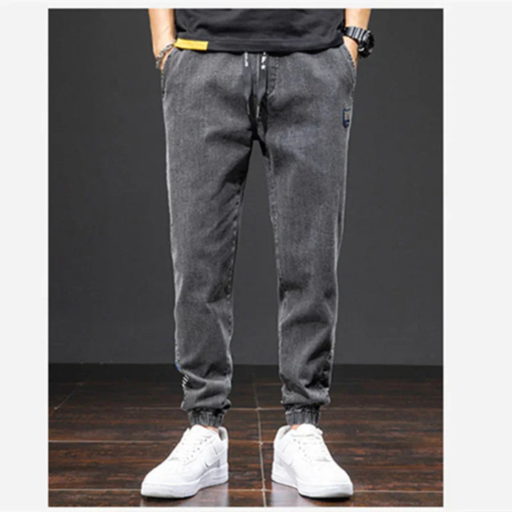 Men's gray casual jogger pants with elastic cuffs and white sneakers on wooden floor