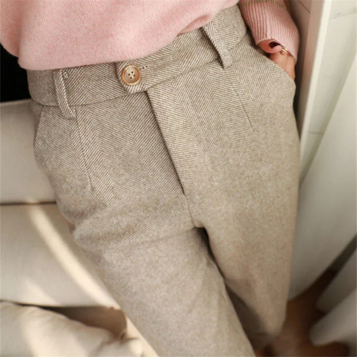 Close-up of beige high-waist herringbone trousers with button detail, worn with a pink sweater