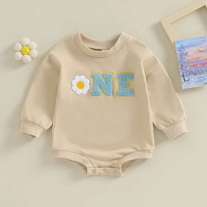 Beige baby bodysuit with long sleeves, ribbed cuffs, and 'ONE' lettering with flower design