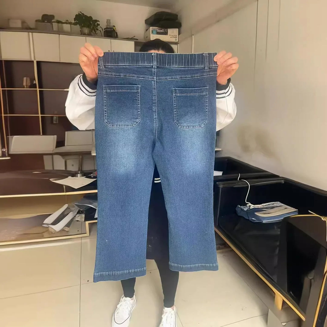 Person holding up a pair of blue denim jeans with back pockets in a modern room