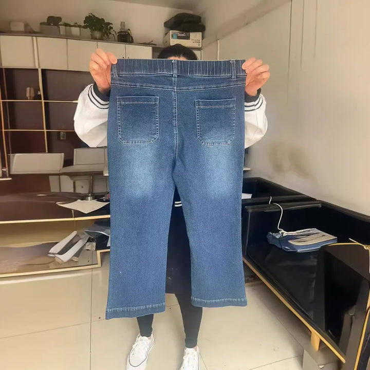 Person holding up a pair of blue denim jeans with back pockets in a modern room