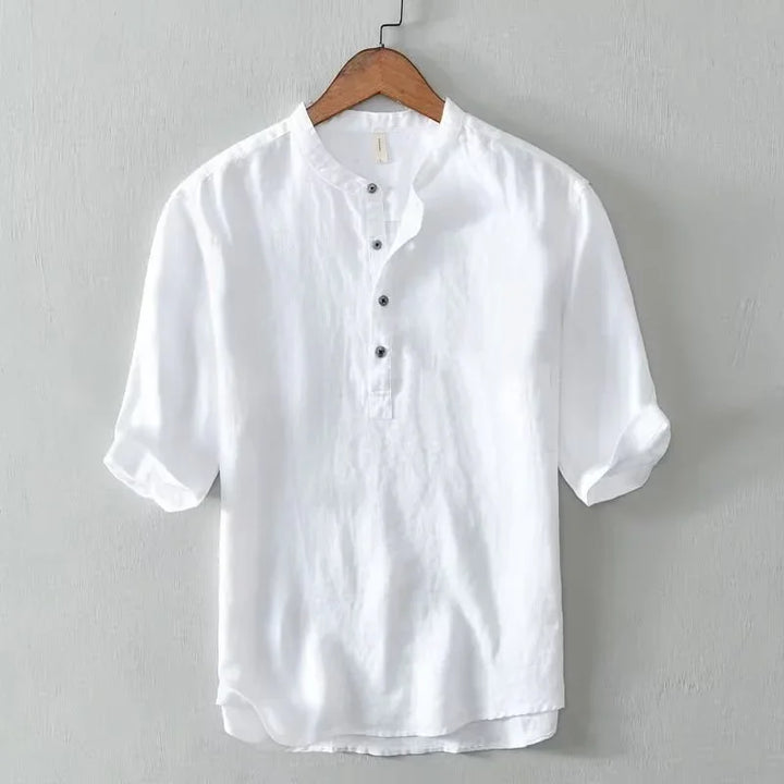 White casual linen shirt with rolled-up sleeves hanging on wooden hanger against gray wall