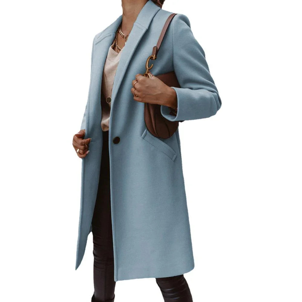 Woman wearing light blue long coat with black button, beige top, black pants, and brown shoulder bag