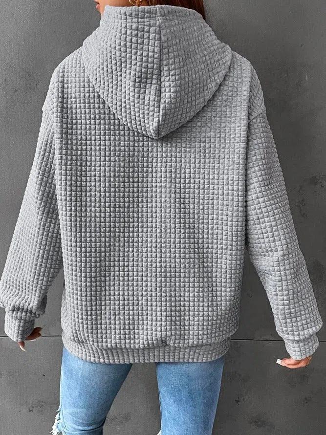 Back view of a person wearing a textured gray waffle-knit hoodie with blue jeans against a gray wall
