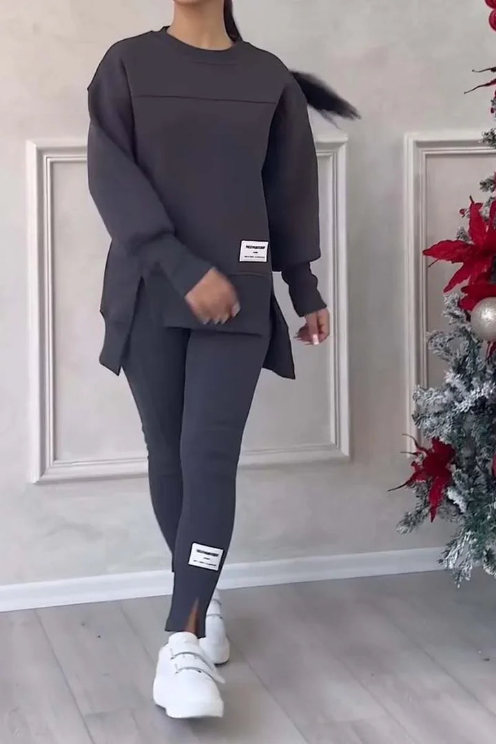 Woman wearing dark gray oversized sweatshirt and leggings with white sneakers walking indoors near decorated Christmas tree