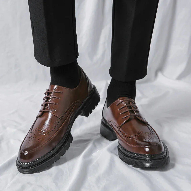Brown leather brogue dress shoes with black soles worn with black pants and socks on white background