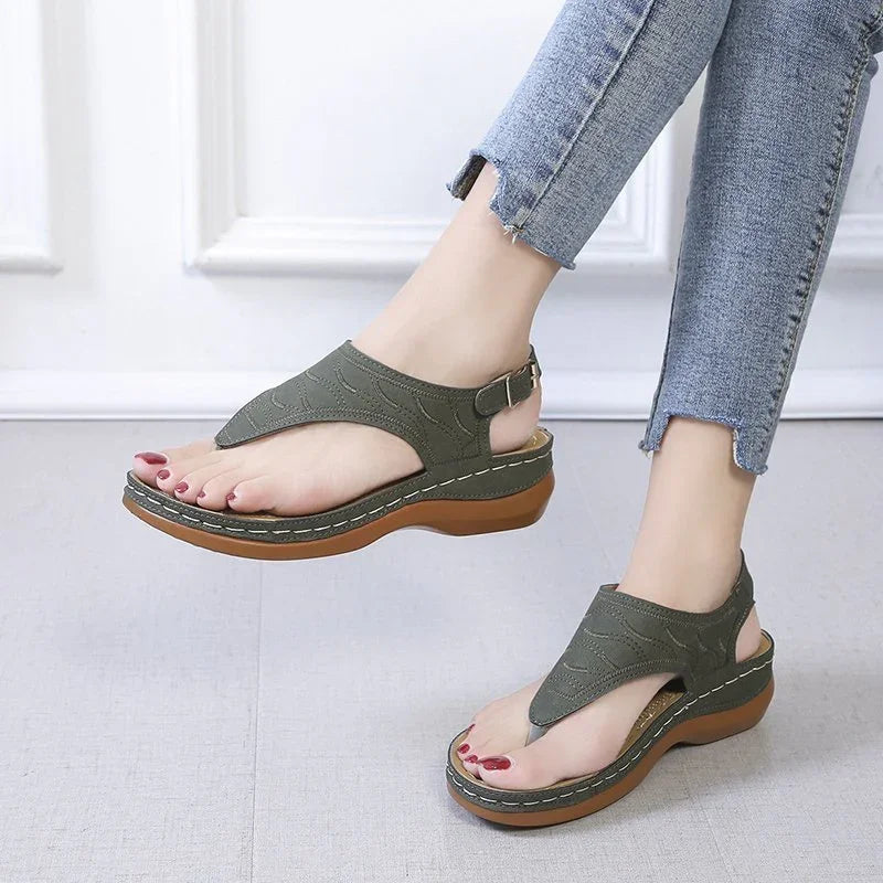 Woman wearing green leather sandals with brown soles and ankle straps, paired with light blue frayed hem jeans