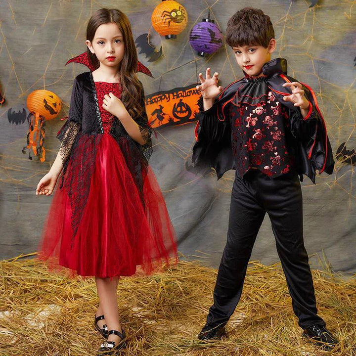 Two children in Halloween costumes, girl in red and black vampire dress, boy in black and red vampire outfit with cape