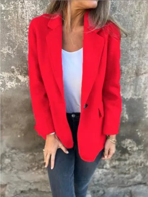 Woman wearing a bright red blazer over a white top and black jeans standing against a textured wall