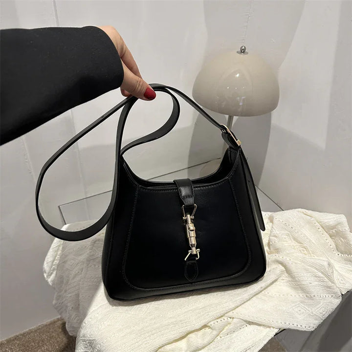 Hand holding black leather handbag with silver clasp over white textured cloth and modern beige lamp