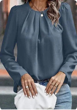 Woman wearing a long-sleeve blue blouse with pleated details, paired with jeans and holding a white clutch