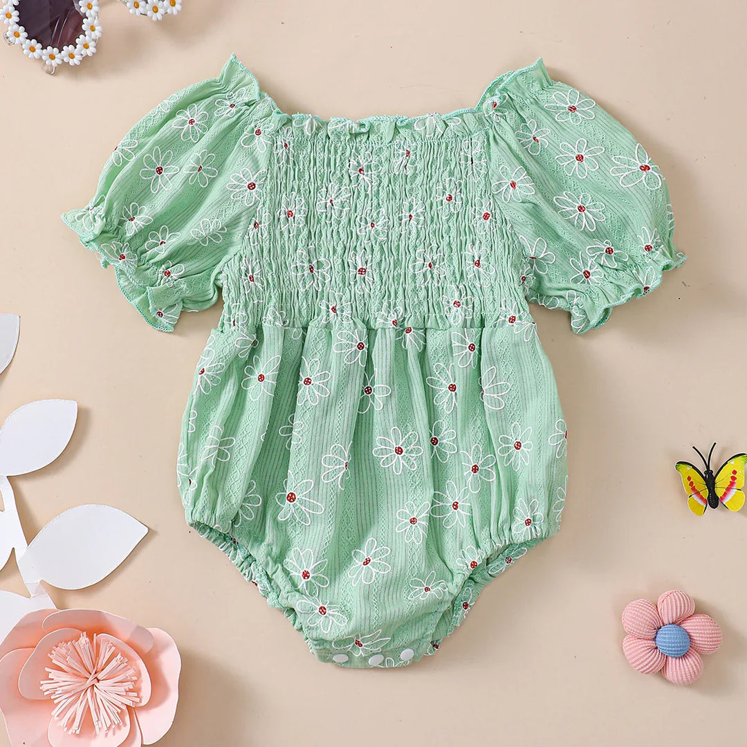 Mint green baby romper with white daisy print, puff sleeves, and snap buttons on beige background