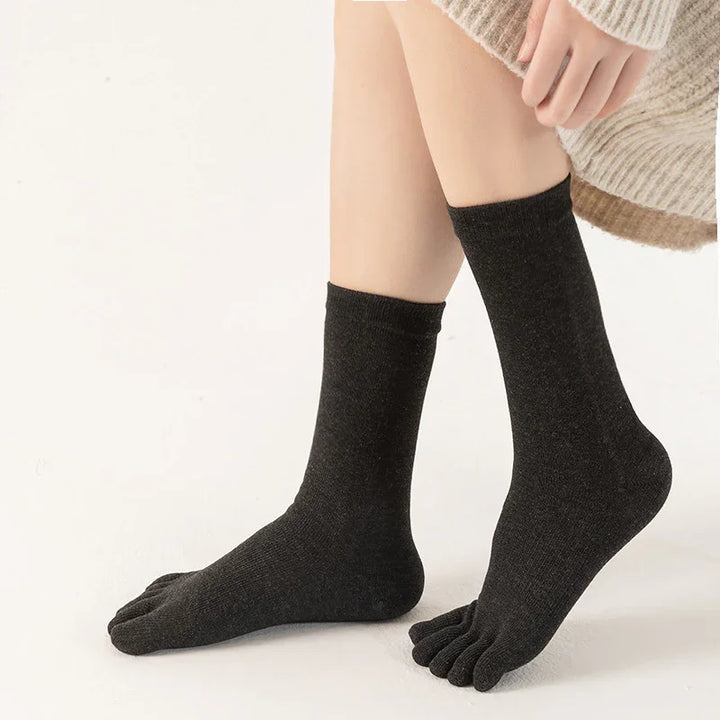 Person wearing black toe socks with a beige knit sweater on a neutral background