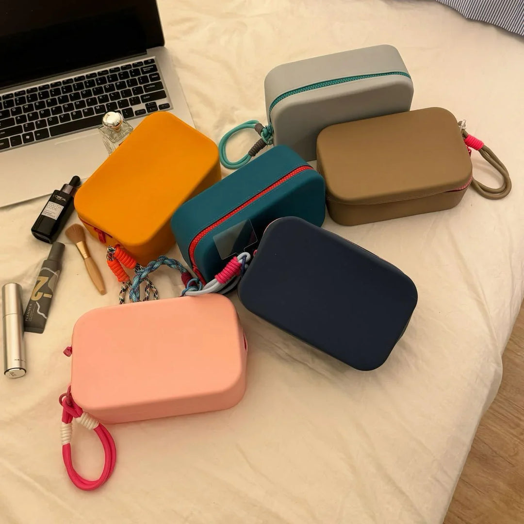 Colorful rectangular cosmetic bags with zippers on a bed next to makeup items and a laptop