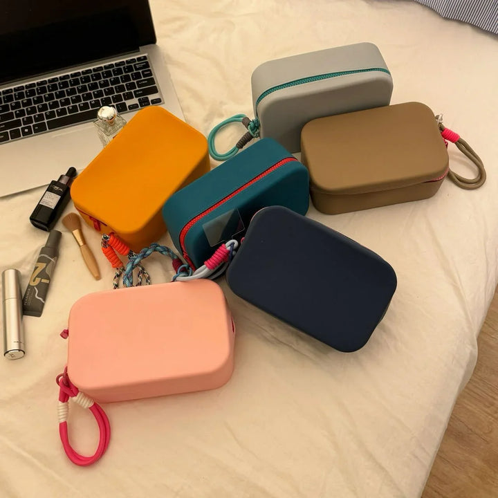 Colorful rectangular cosmetic bags with zippers on a bed next to makeup items and a laptop