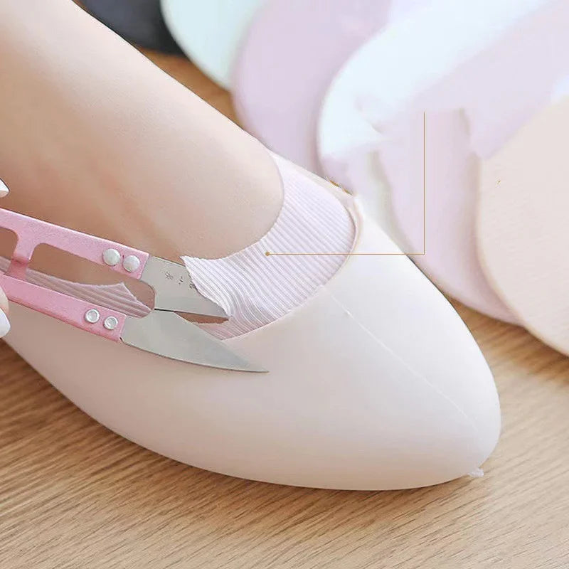 Close-up of hand cutting pink no-show sock with scissors inside white flat shoe on wooden floor