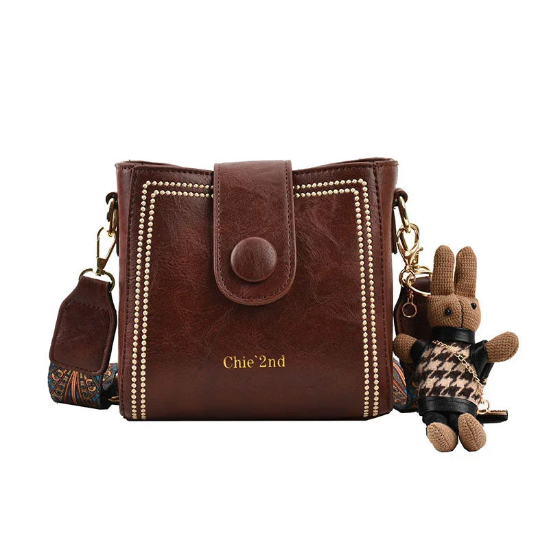 Brown leather Chie'2nd handbag with studded design and detachable patterned strap, featuring a small stuffed bunny keychain