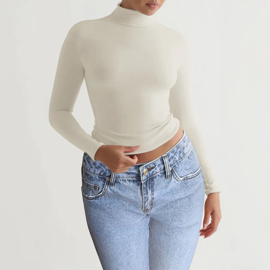 Woman wearing beige turtleneck long sleeve top and light blue high-waisted jeans on white background