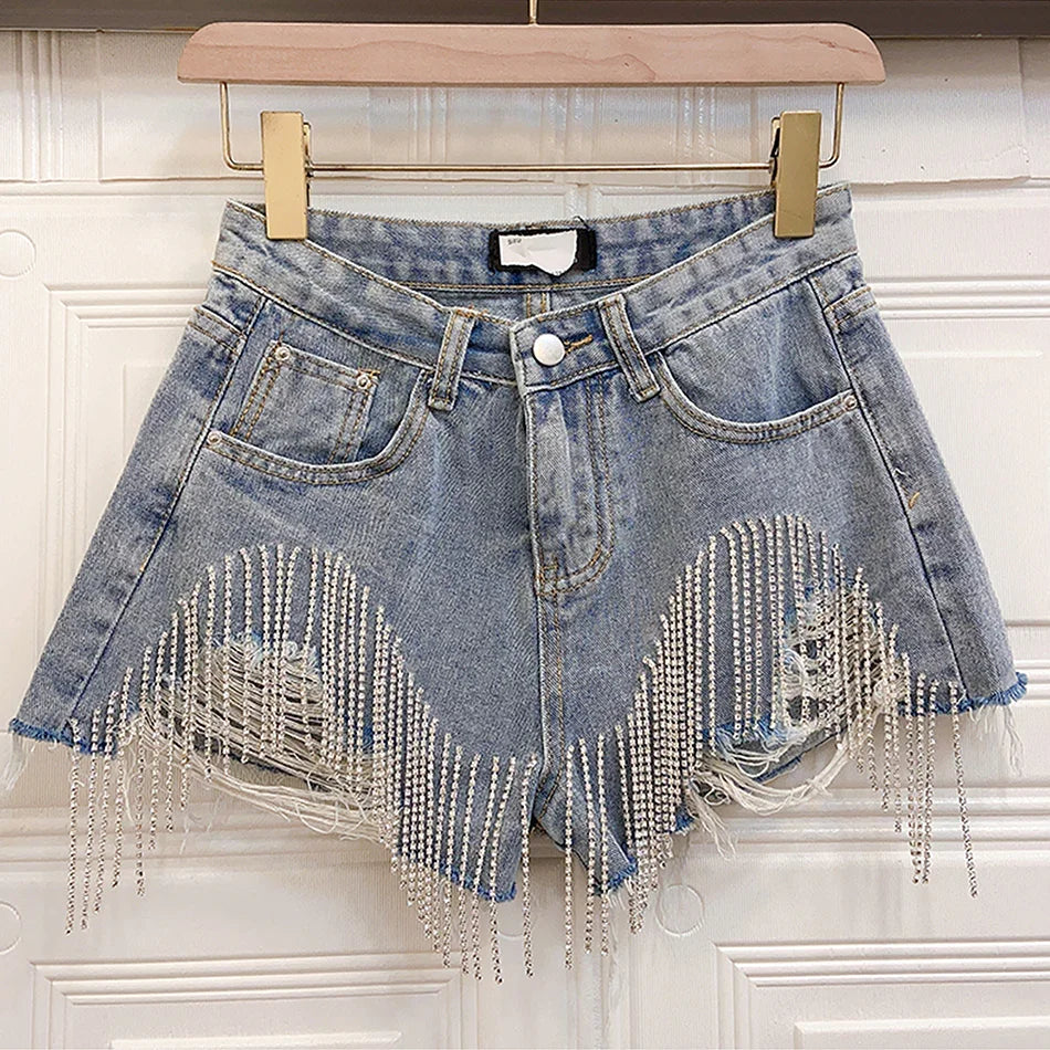 Distressed denim shorts with silver rhinestone fringe hanging on wooden hanger