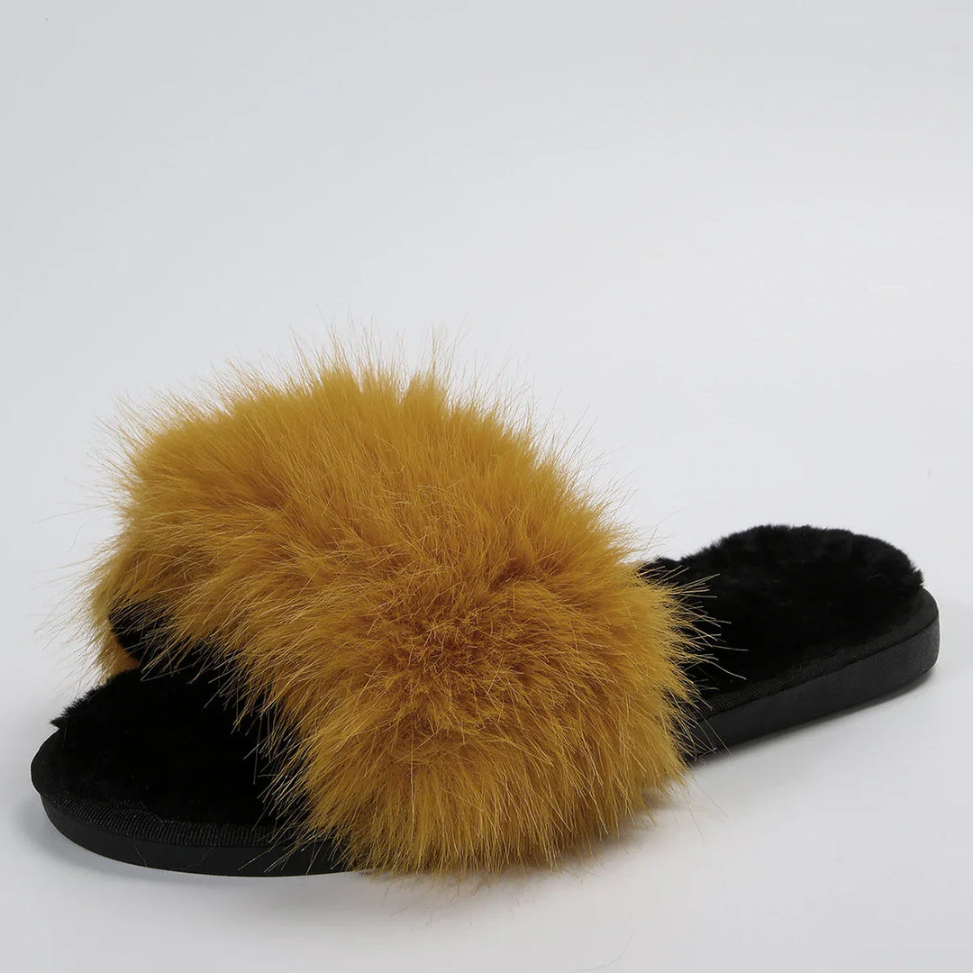 Black fuzzy slipper with large fluffy mustard yellow fur strap on plain background