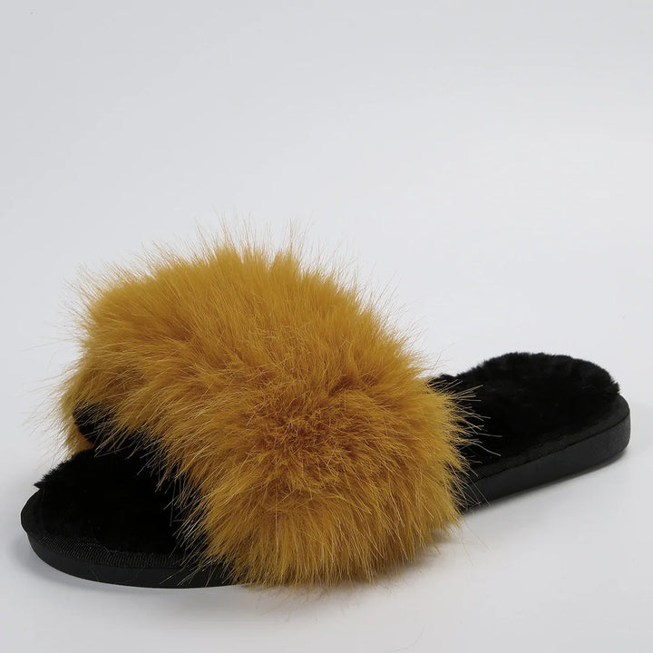 Black fuzzy slipper with large fluffy mustard yellow fur strap on plain background