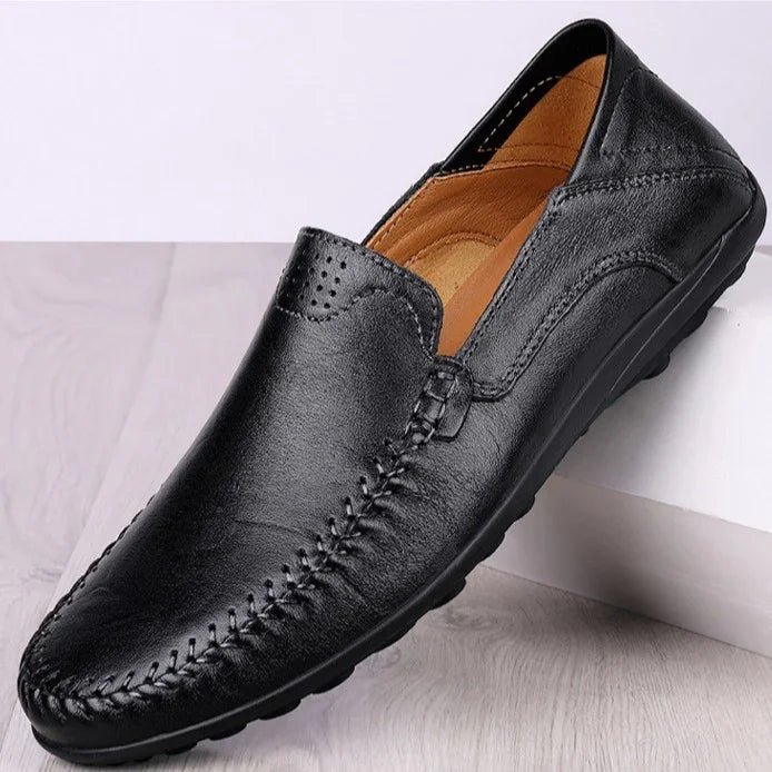 Black leather men's loafer with moc toe stitching and cushioned tan interior on wooden surface