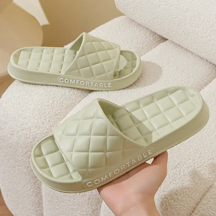 Light green quilted comfort slides with cushioned sole displayed on beige fabric surface