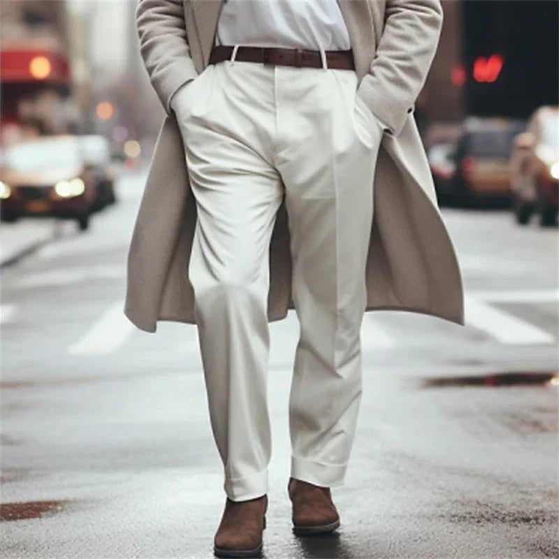 Man wearing beige trench coat, white pants, brown belt, and brown boots walking on city street