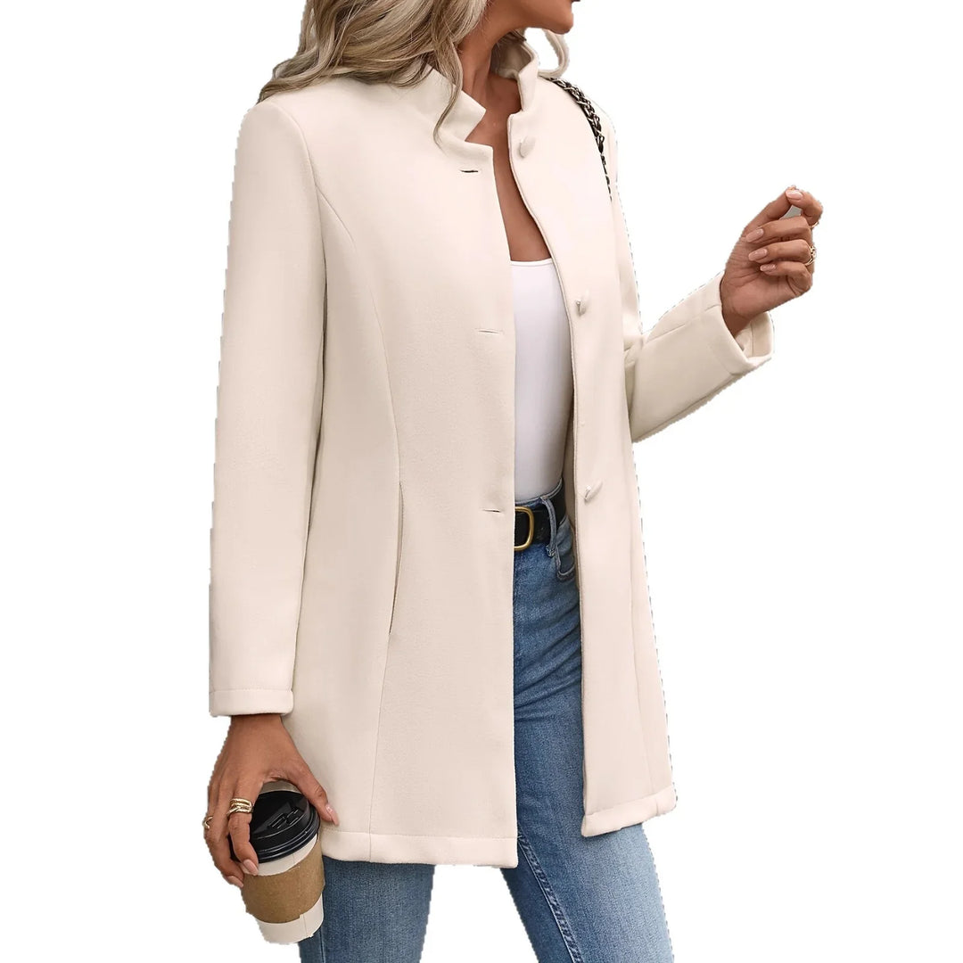 Woman wearing beige button-up coat with blue jeans and white top holding coffee cup