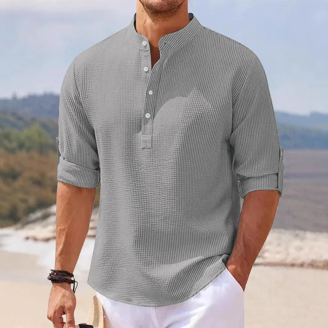 Man wearing casual grey textured henley shirt with rolled-up sleeves on a beach background